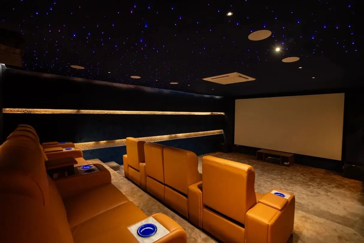 Private luxury home theater with fiber-optic starlight ceiling, tiered recliners, and backlit wall reveals
