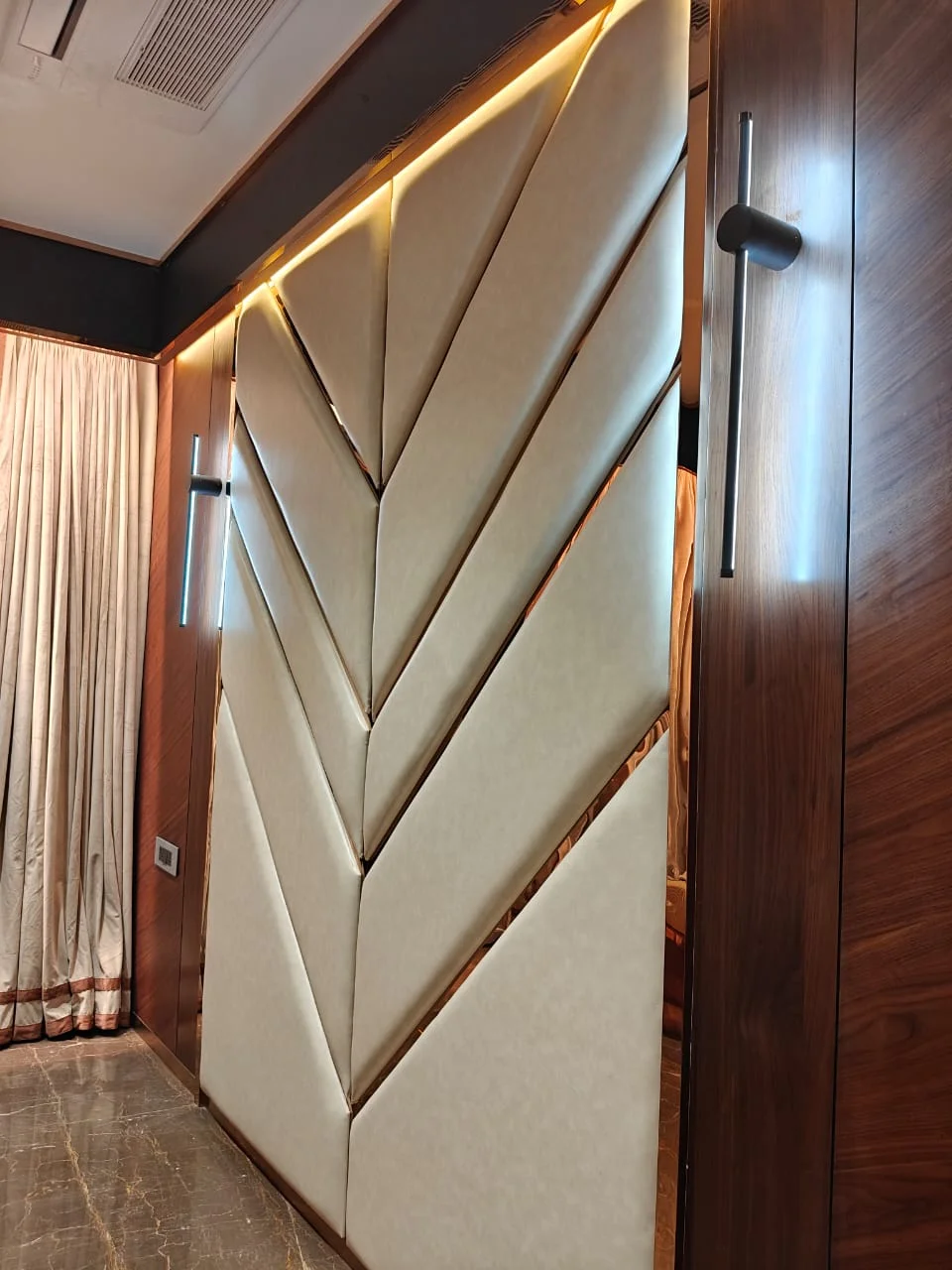 Full-height geometric chevron upholstered acoustic wall paneling with rose-gold metallic T-profile inlays and cove lighting